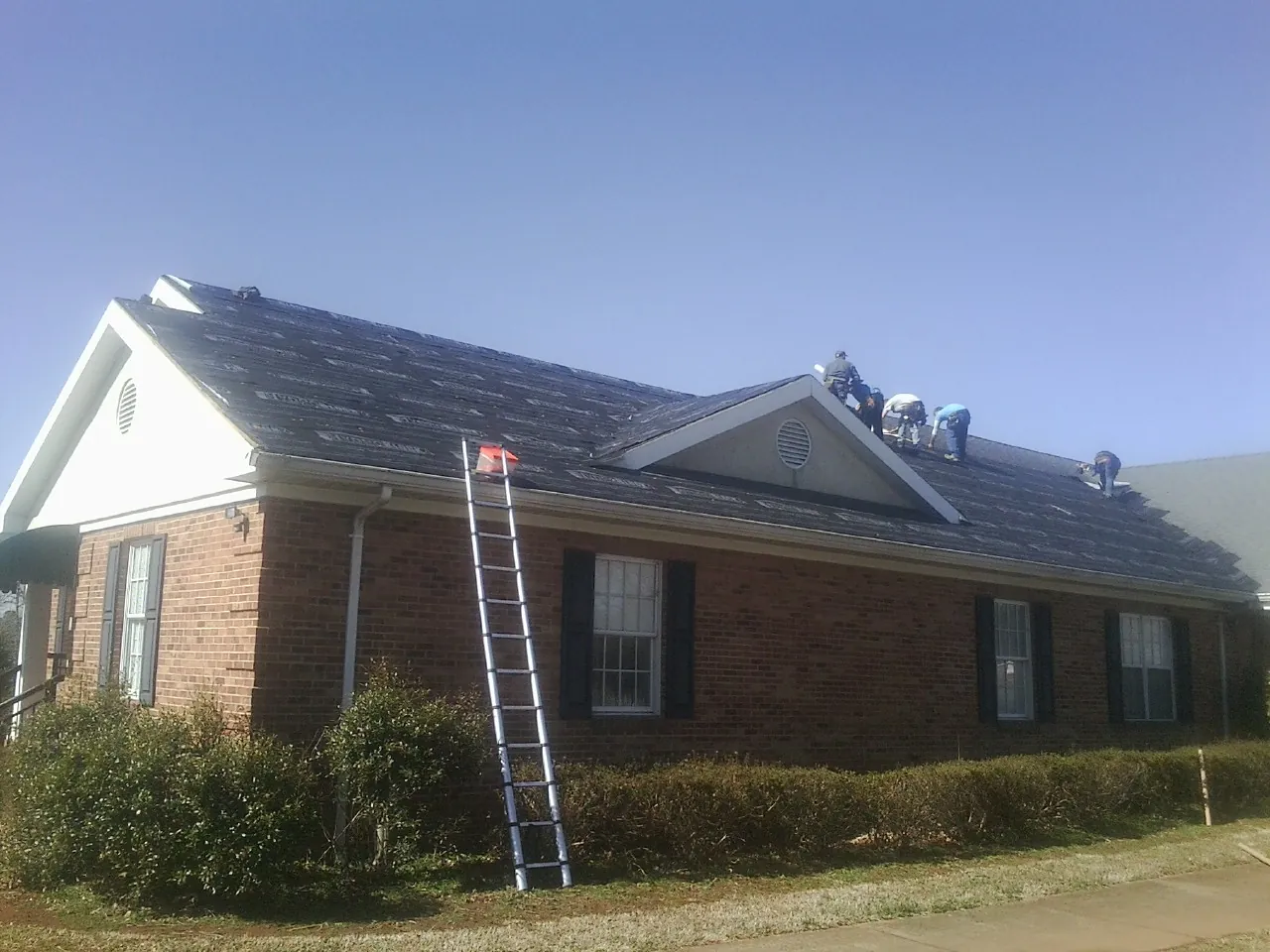 Crew tearing shingles off a brick ranch roof with a ladder set — Metal Roof Repair work by our crew in Molalla