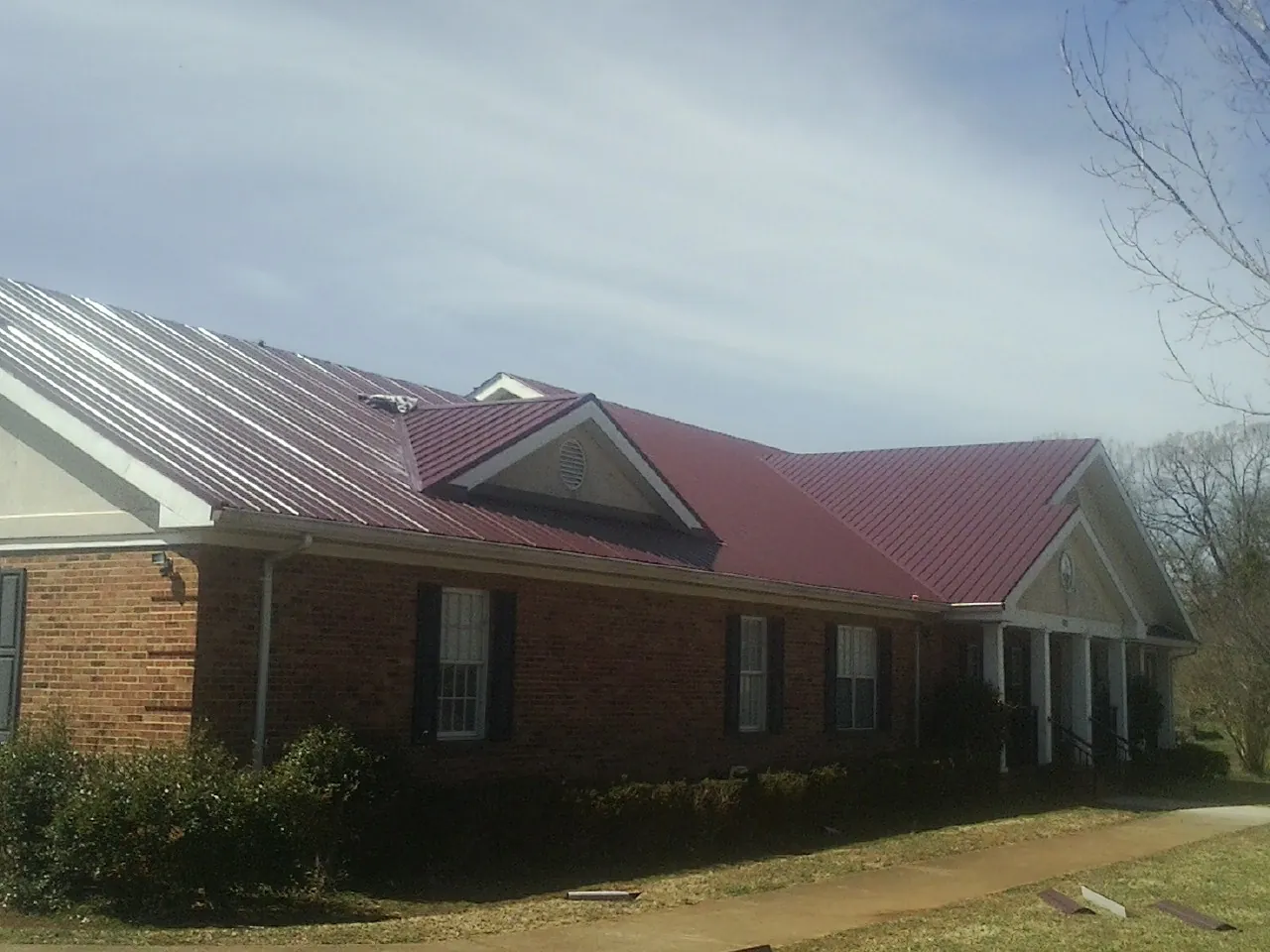 Red metal roof with gabled entries on a long brick building, from a Hail Damage Roof Repair job in Molalla