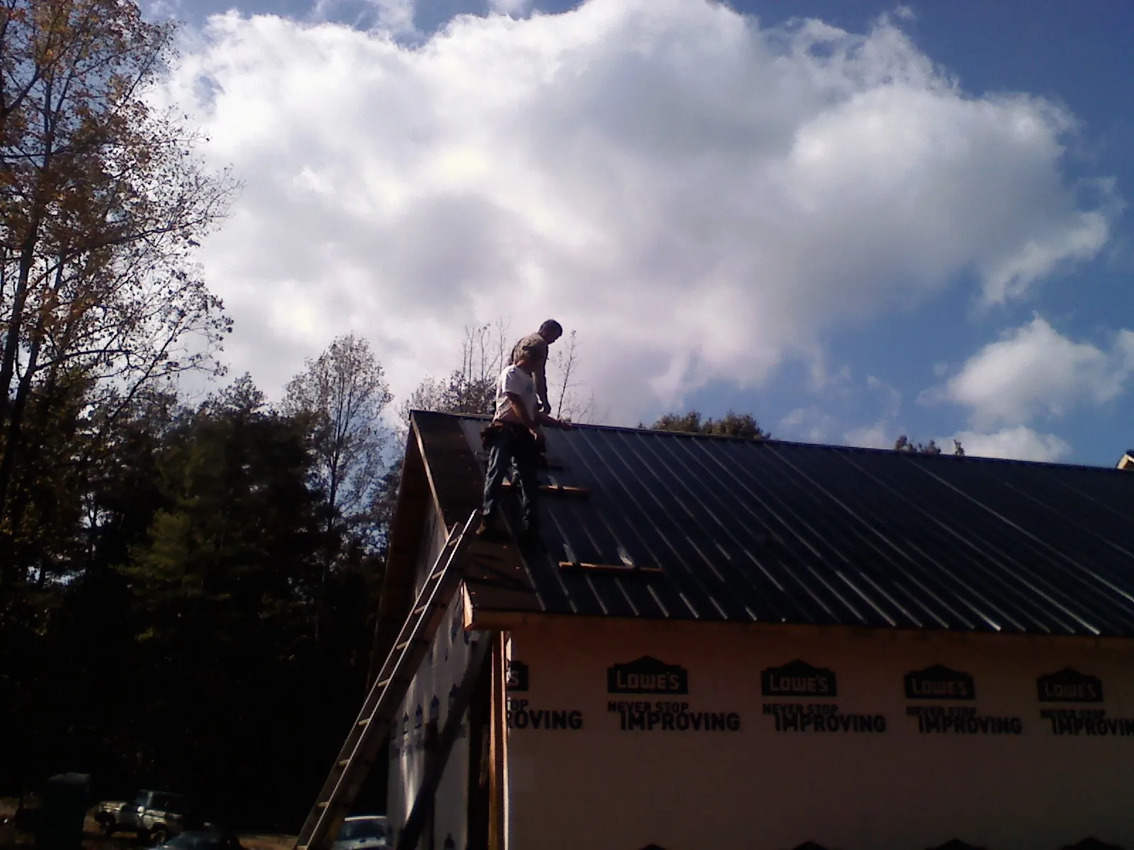 Roofer fastening dark metal panels high against a cloudy sky, from a Roof Inspection job in Molalla