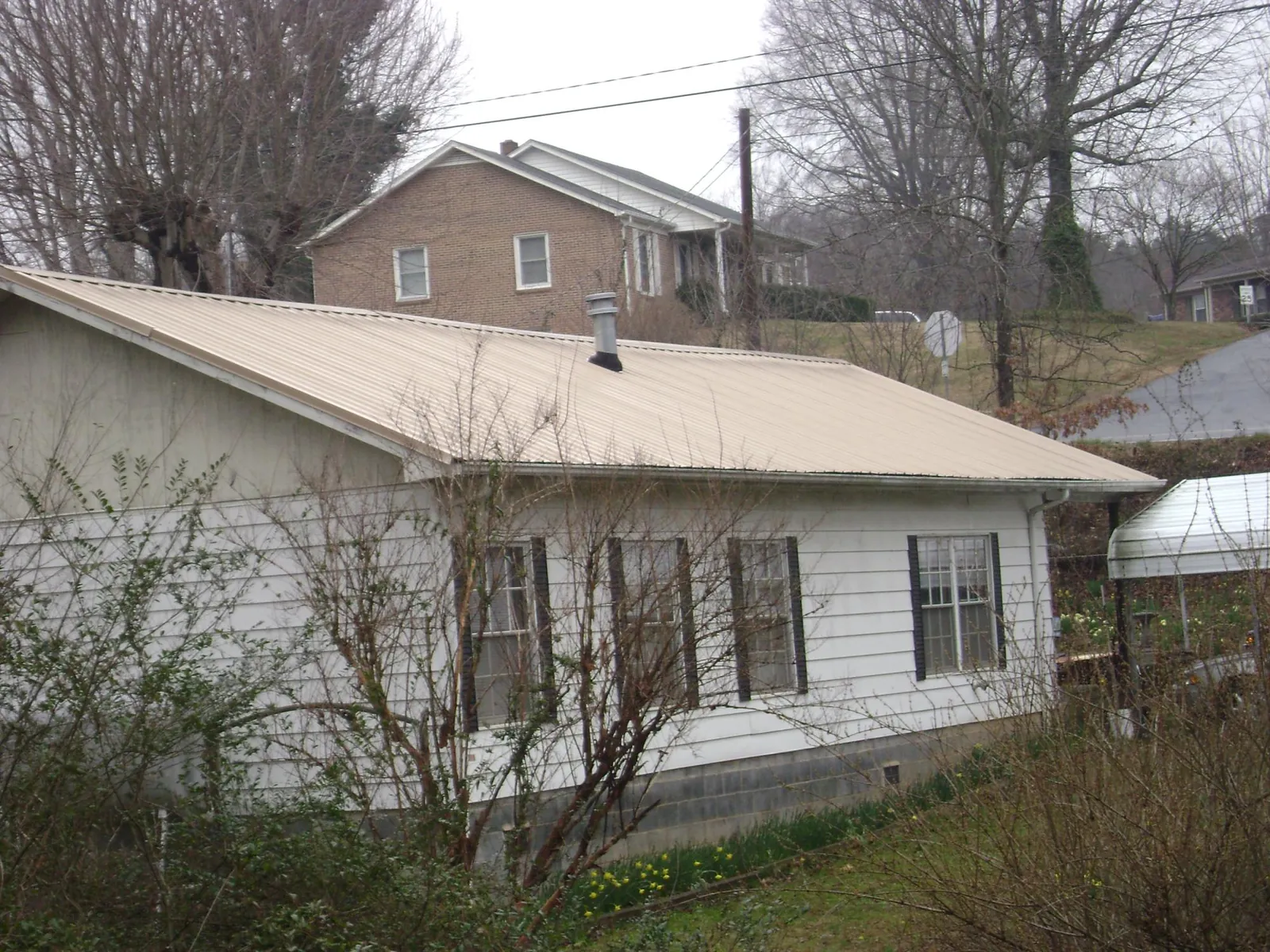 Tan metal roof on a white sided house set into a hillside — Commercial Roofing by Roofing Brothers in Molalla